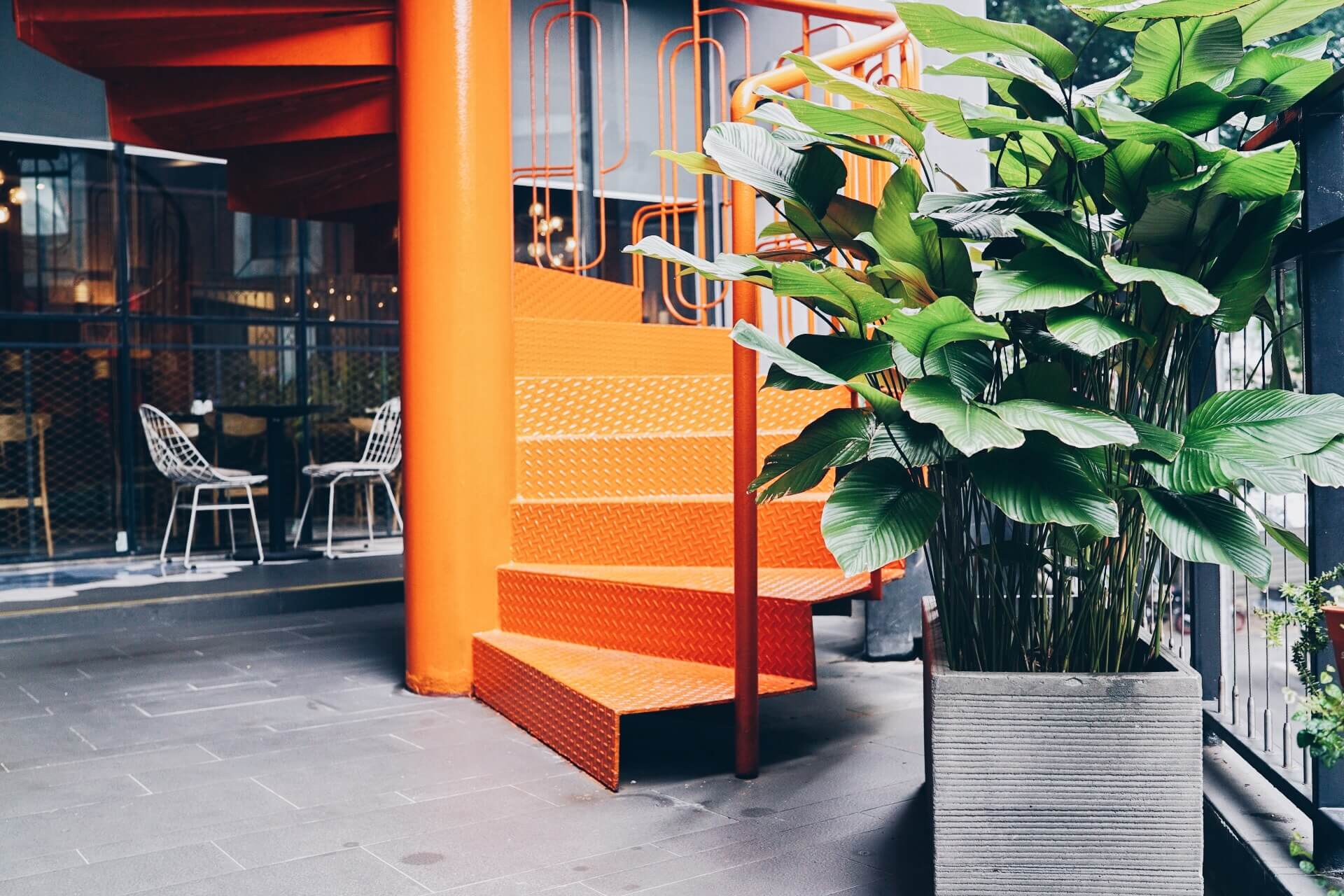 Potted plant next to a neon orange spiral staircase at the KL Journal Hotel