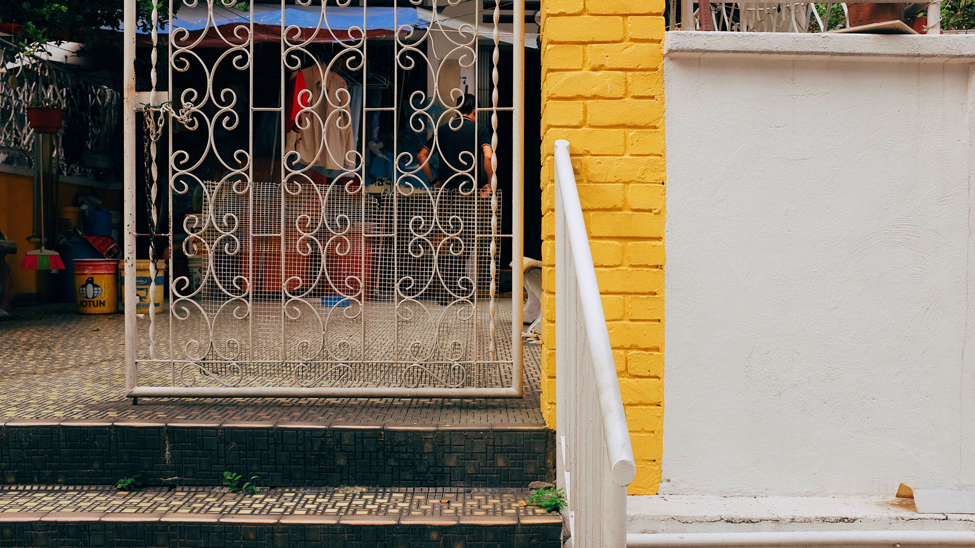 Metal swing gate with patterns next to a yellow and white wall